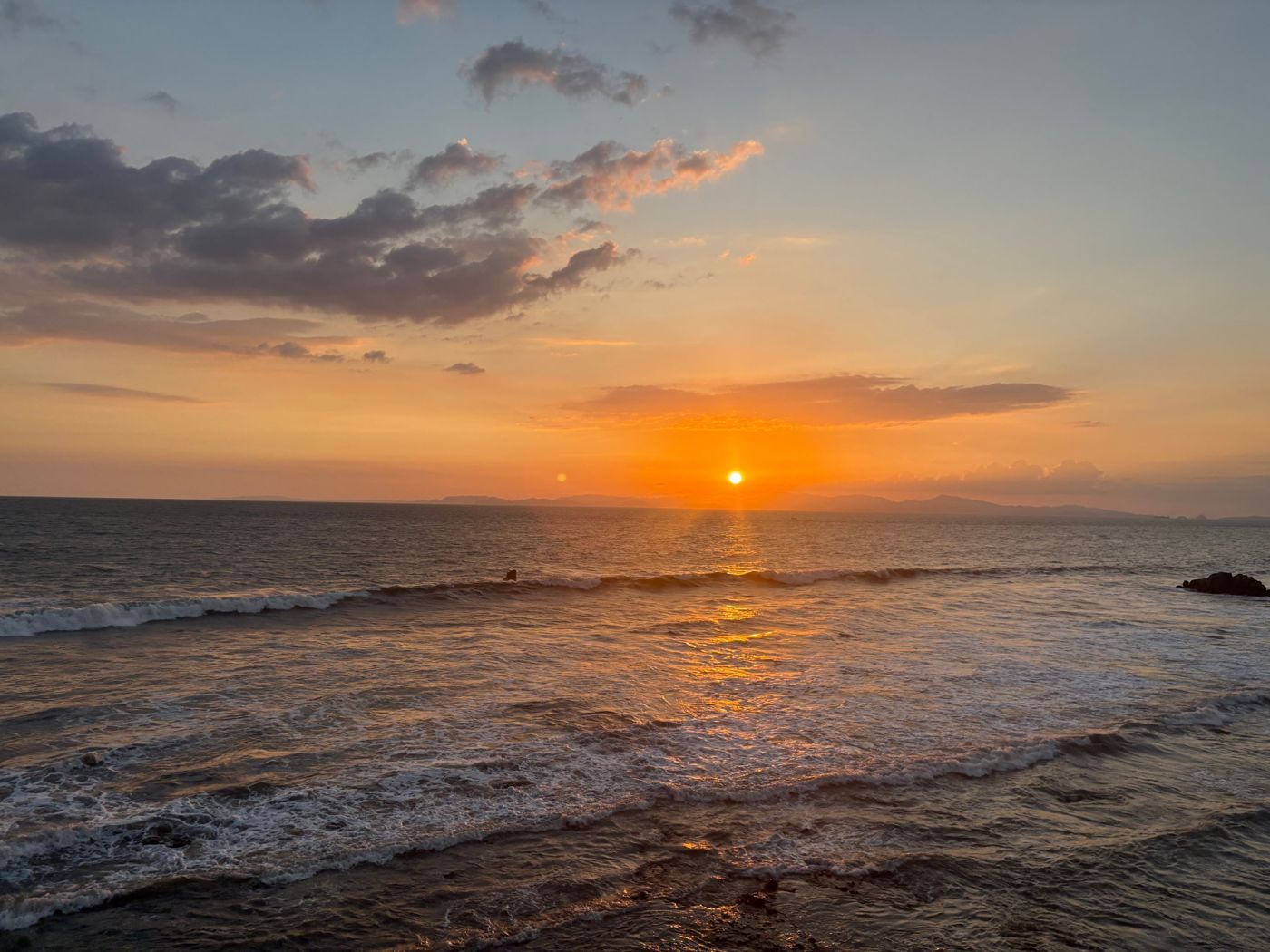 The sun setting over the Pacific Ocean with waves in the foreground